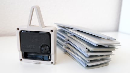 The clock mechanism (movement) on the left; the plug-in pieces on the right. A sheet of paper between the plastic pieces prevents them from getting scratched during transportation.