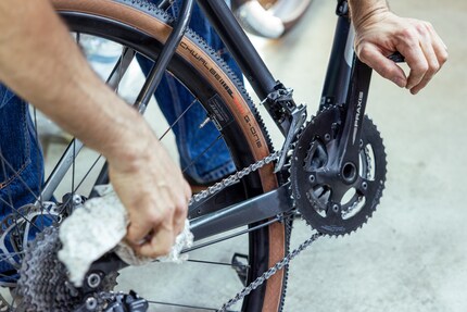 Elia presst sich den Sattel in den Bauch, bringt über das Pedal Spannung auf die Kette und reibt diese sauber.